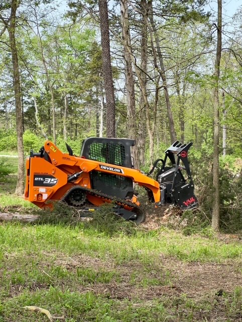 Develon skid-steer clearing woods — action shot