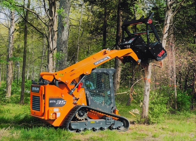 Orange Develon skid-steer forestry mulching in spring woods